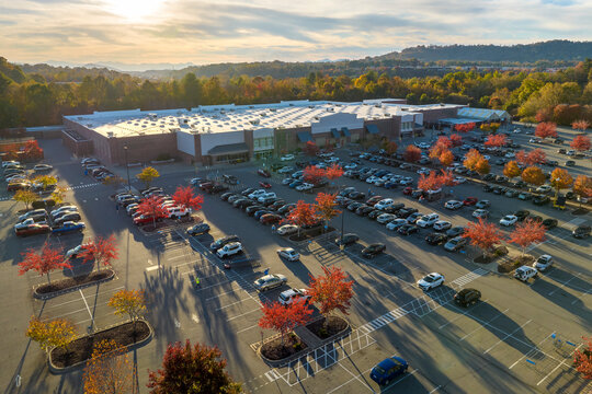 View from above of american grocery store with many parked cars on parking lot with lines and markings for parking places and directions. Place for vehicles in front of a strip mall center