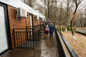 Father with three kids on terrace of one-storey modular houses in spring rainy forest.