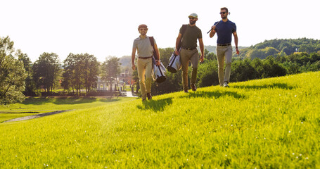 Three handsome male friends in sunglasses strolling with their clubs and golf bags