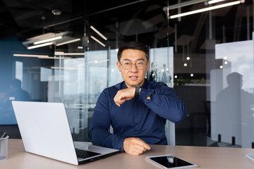 Successful businessman inside office, using app on smart watch to communicate, asian man giving...