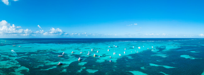 Aerial panorama of many anchoring yachts and tourist boats in the turquoise Caribbean sea. Clear blue sky on the horizon. Best destination for vacation in Punta Cana