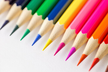 Fototapeta premium Colored pencils rainbow laid out side by side one to other on white background, rod writing material, close-up selective focus