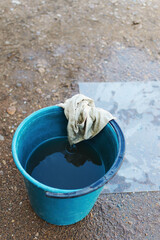 Angle top view outdoors on the ground there is a blue bucket with dirty water and an old wet shabby rag on it, copy space.