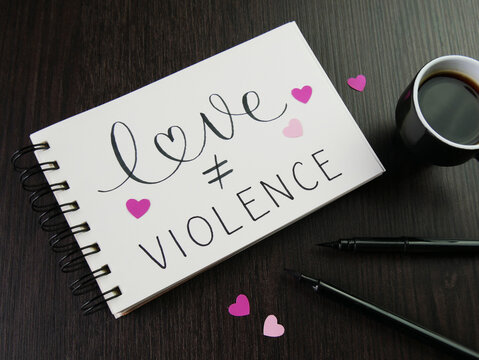 LOVE ≠ VIOLENCE lettering in notepad with pink hearts, cup of espresso and pens on desk