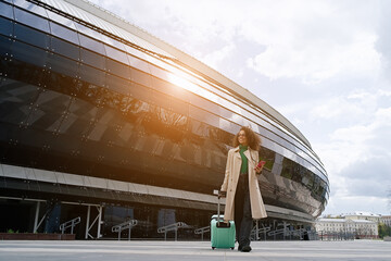 Young african woman walking outdoors carrying a suitcase and going to travel by airplane at modern...