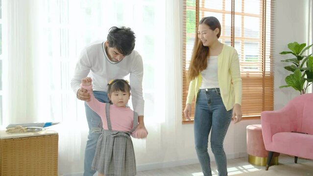 Happy asian family mother stepfather and child daughter dancing to music in living room at home, enjoying funny weekend