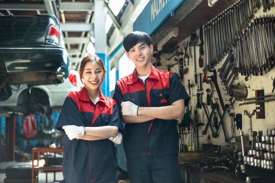 Asian  automotive engineer people wear helmet work in mechanics garage.young auto mechanic in uniform is looking at camera and smiling examining car.