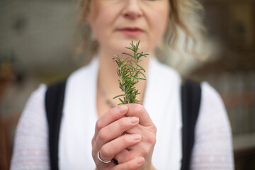 Portrait of blonde woman smelling rosemary leaf while standing in the garden