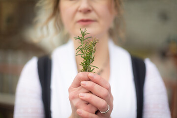 Portrait of blonde woman smelling rosemary leaf while standing in the garden