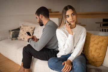 Busy sad young arab man typing on smartphone, ignoring european wife calling by phone