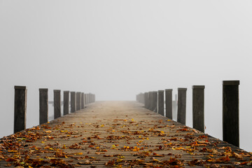 Jetty in the fog. Mystical foggy landscape at the lake. Morning fog in autumn.
