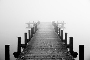 Jetty in the fog. Mystical foggy landscape at the lake. Morning fog in autumn.
