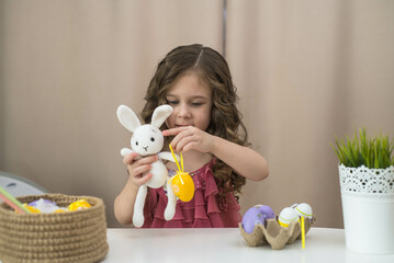 little girl playing with easter bunny and easter eggs on white table in light bedroom.