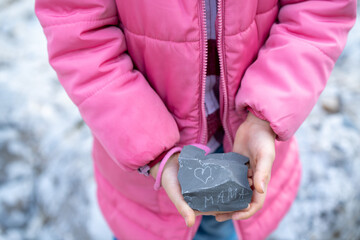 A girl in a pink jacket is holding a rock that says Mom