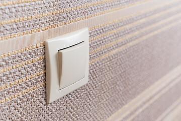 White light switch on the wall with brown wallpaper. 