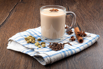 Glass cup with masala chai, cinnamon, star anise and cloves with cardomom on a kitchen towel.