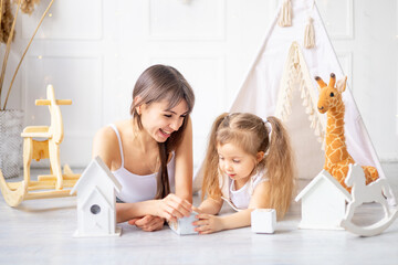 mom and little baby daughter are playing at home in a bright children's room among wooden toys, smiling and having fun, happy motherhood