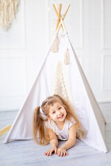 a small child girl looks out of the wigwam at home in a bright children's room and laughs © Any Grant