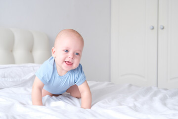 smiling boy with big blue eyes in a bodysuit learns to crawl on white bedding. Healthy newborn baby