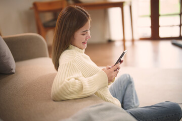 Obraz premium Happy asian woman using&nbsp;mobile phone and receiving&nbsp;good news.on sofa at living room.