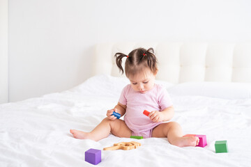 Fototapeta premium funny baby girl in pink bodysuit playing with children wooden cubes toys on bed