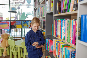 Child schoolboy reading book in library or bookstore. Concept of back to school and education.