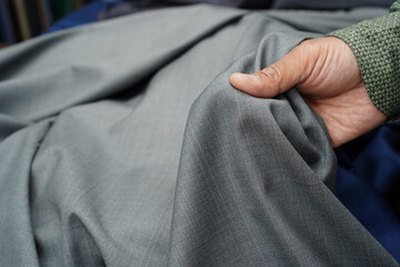 Obraz na płótnie Canvas A man's hand holding a piece of quality silver grey fabric. Choosing a textile material in a tactile and visual way to tailor a garment, trouser, jacket. Close-up, selective focus, blurred background.