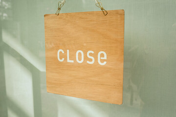 A light brown wooden board with the inscription ' CLOSE ' hangs in front of a mint colored wall.