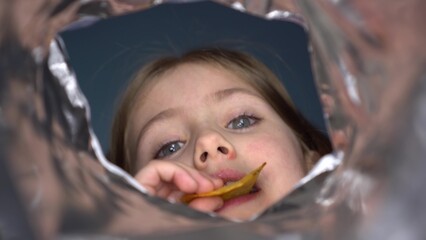 The girl looks into a pack of snacks and eats. The child eats chips from a pack. First-person view...