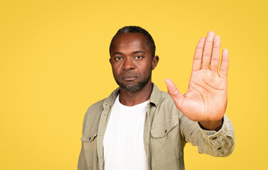 Cerious calm confident middle aged black male in casual showing hand palm, making stop gesture