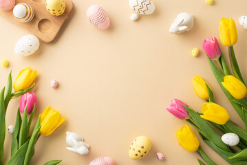 Fototapeta na wymiar Easter decor concept. Top view photo of colorful easter eggs ceramic bunnies yellow and pink tulips and wooden egg holder on isolated pastel beige background with copyspace in the middle