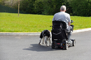 Walking your dog, disabled man in mobility scooter enjoys the freedom it allows him to be able to walk his pet spaniel dog despite his disability.