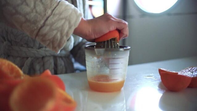 Woman using orange juicer, squeezer, reamer preparing an orange juice at home.