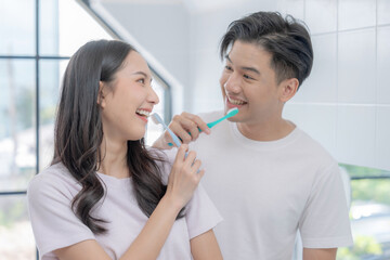 Happy Asian couple brushing their teeth together in the bathroom.