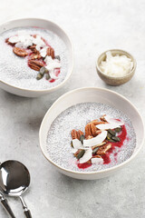 Breakfast idea - two bowls with with chia seeds pudding, red raspberry smoothie, pecan nuts, coconut flakes and pepitas on gray background