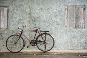 Naklejka na ściany i meble Vintage bicycle on old rustic dirty wall house, many stain on wood wall. Classic bike old bicycle on decay brick wall retro style. Cement loft partition and window background.