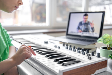 A girl learns to play the piano with a teacher online, remote learning music.