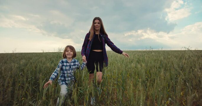 Mother holding her daughter's hand for a walk through a green field. Happy family smiling together and spending time together. Carefree loving from parents in childhood. High quality 4k footage