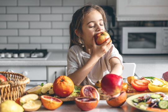 Funny little girl eating apples in the kitchen, health and nutrition concept.