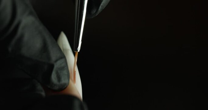 pasting a sticker with a pattern on a nail in a beauty salon. the master makes a manicure on a black background. vertical video