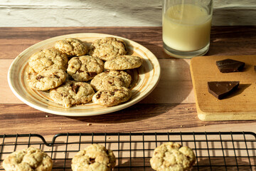Plate with several chocolate chip cookies illuminated by the light from a window.