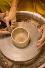 Hands of young woman master of ceramics working on a potter's wheel, making plate of clay in own art studio. Close up, top view