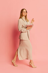 Happy young pretty blonde girl, student wearing modern office style clothes using tablet over pink background. Concept of youth, student college life, business and education.