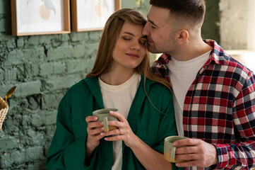 Close-up of a man kissing his wife on the forehead, both holding cups of coffee.