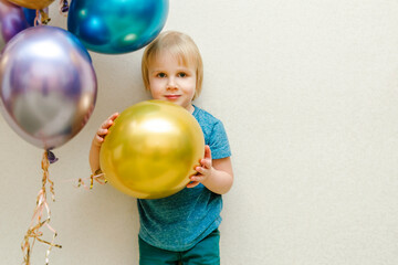 Fototapeta na wymiar Blond cute happy Child kid boy celebrating third birthday with colorful balloons at party,home in front of wall.baby smiling looking at camera.adorable caucasian baby.Festive background decoration