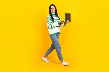 Full length photo of stunning glad lady wear trendy clothes going empty space hold netbook isolated on yellow color background