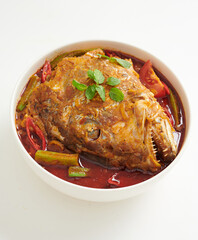 Curry fish head with lady's finger and tomatoes in a wok. A malaysia cuisine with Indian influence. Top view isolated on white background