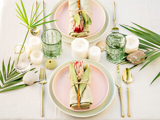 A beautiful floral table arrangement. Pastel crockery and golden cutlery make a luxury setting. The  composition of flowers and candles create a romantic atmosphere, perfect for a date or a wedding. - obrazy, fototapety, plakaty
