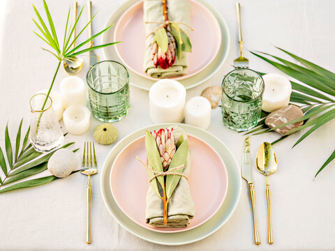 A beautiful floral table arrangement. Pastel crockery and golden cutlery make a luxury setting. The  composition of flowers and candles create a romantic atmosphere, perfect for a date or a wedding.
