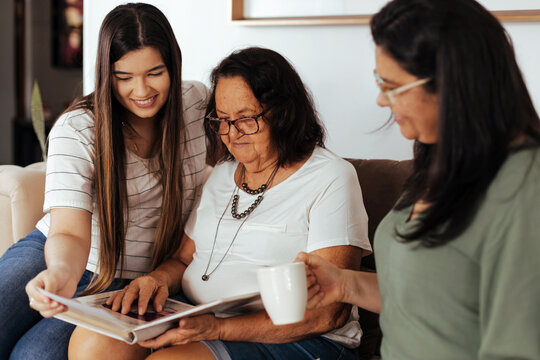 Three generation family looking at old photo album in living room. - Powered by Adobe